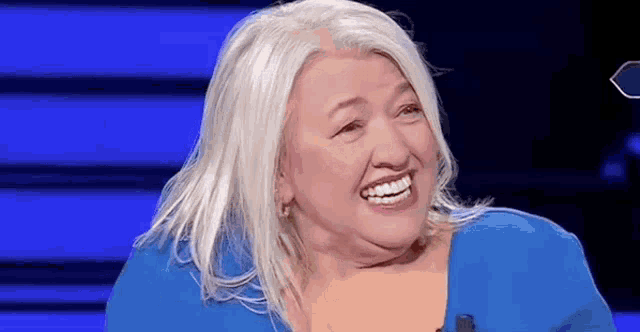 a woman with white hair is smiling while sitting on a stage .