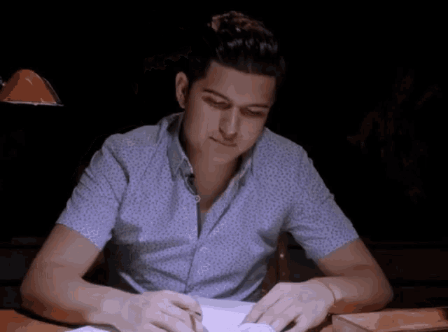 a man in a blue shirt is sitting at a desk in a dark room .