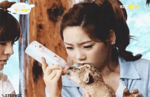 a woman feeding a baby lion from a bottle with kbs in the background