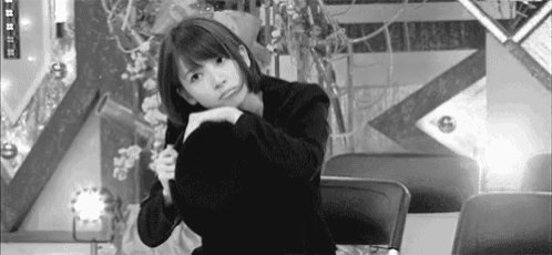 a black and white photo of a woman sitting in a chair with her hands on her hips .