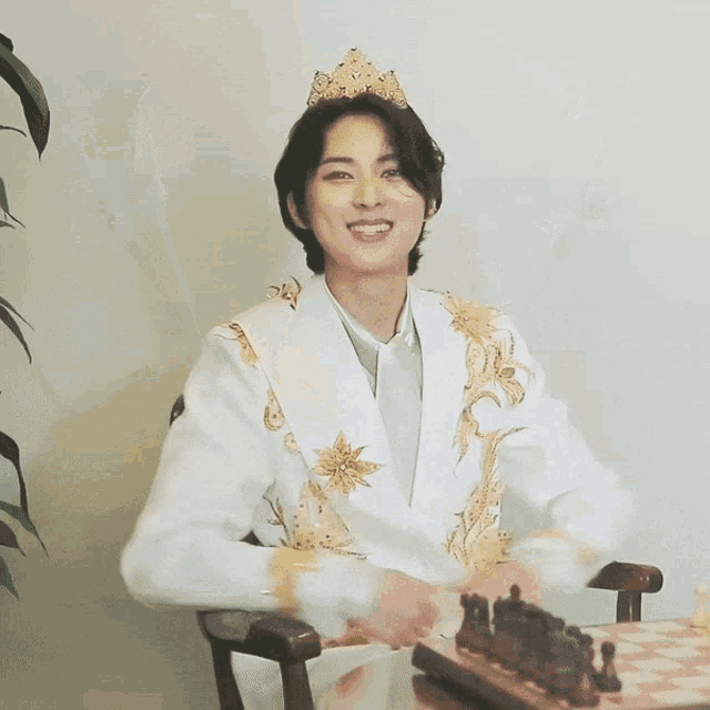 a man wearing a crown is sitting in a chair with his hands in the air