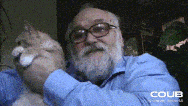 a man with glasses and a beard is holding a cat in his arms with a coub logo behind him