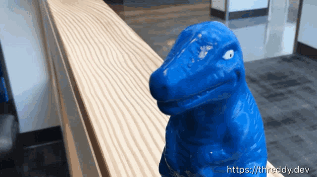 a blue dinosaur statue sits on a wooden railing with the website https://threddy.dev in the corner