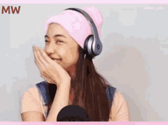 a girl wearing headphones and a pink beanie laughs