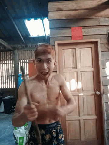 a shirtless man is standing in front of a wooden door with a bag of fertilizer in the background