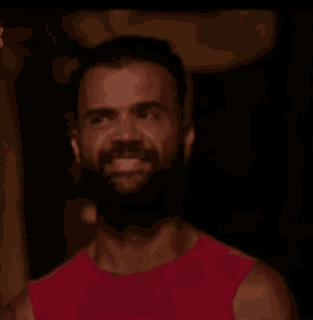 a man with a beard and earring is wearing a red tank top .