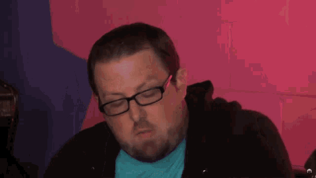 a man wearing glasses and a blue shirt with the letter m on it