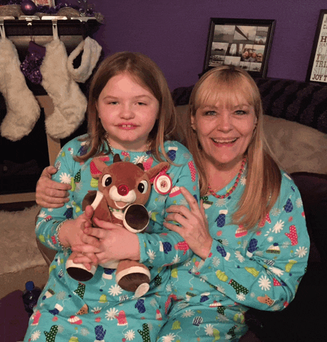 a little girl is holding a stuffed reindeer while sitting next to a woman in matching pajamas