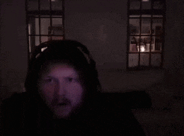 a man with a beard wearing headphones is saluting in a dark room .