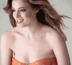 a woman wearing a strapless orange top smiles with her hair blowing in the wind