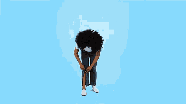 a woman with curly hair is standing on a blue background with her head in the air .