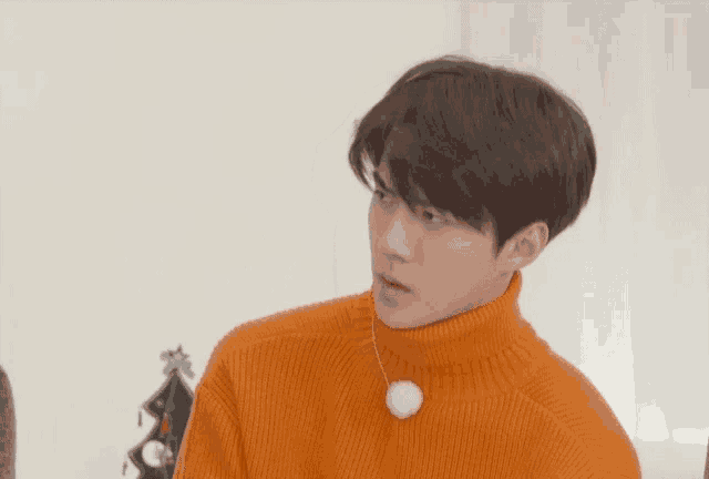 a young man wearing an orange sweater with a white ball on his neck
