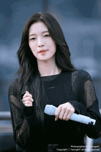 a woman in a black sweater is holding a microphone in her right hand