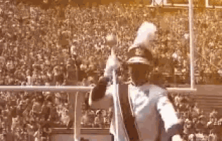 a man in a marching band uniform is holding a trumpet in a stadium .