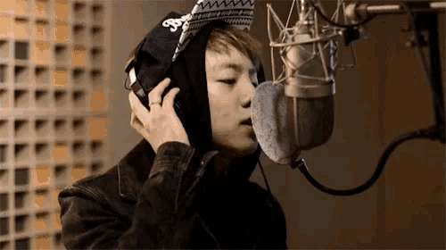 a young man is singing into a microphone wearing headphones and a hat with the letter s on it