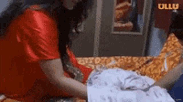 a woman in a red robe is ironing clothes on a bed in a room .