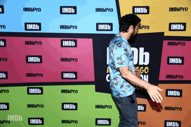 a man in a blue shirt stands in front of a wall that says imdbpro