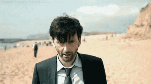 a man in a suit and tie is walking on a sandy beach .