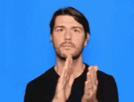 a man in a black shirt is making a prayer gesture with his hands .