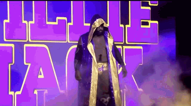 a wrestler in a blue and gold robe is walking out of a ring .