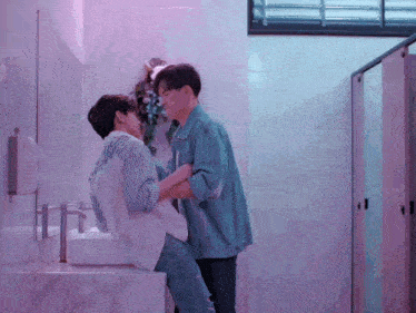 two men standing next to each other in a bathroom with purple walls