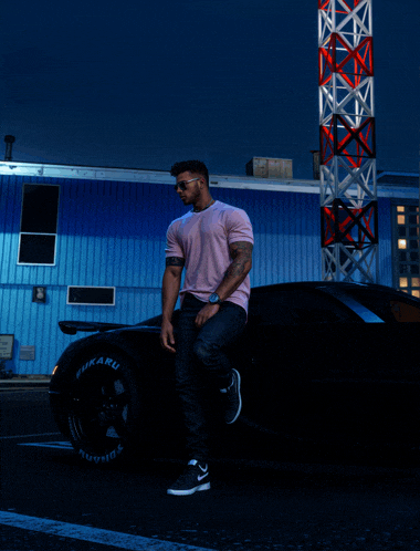 a man in a pink shirt leans on a car with a subaru tire