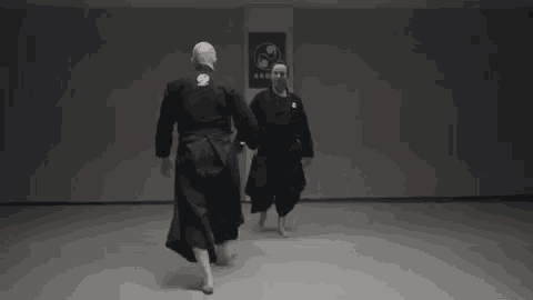 two men are practicing martial arts in a gym while standing next to each other .