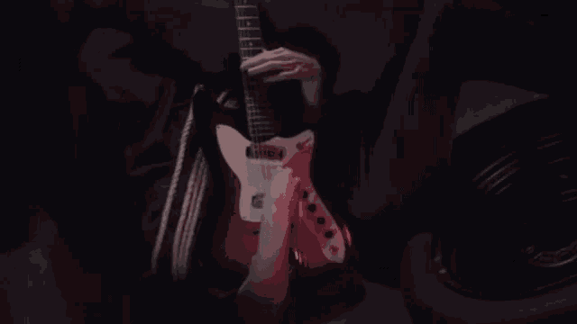 a person is playing a red and white guitar in a dark room .