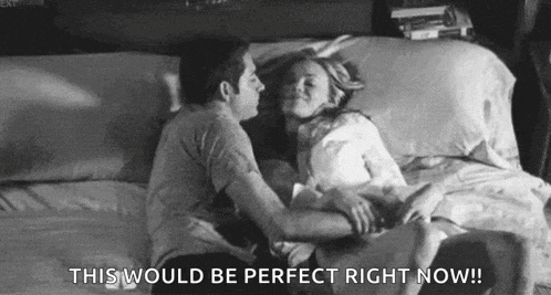 a black and white photo of a man and a woman kissing in bed .