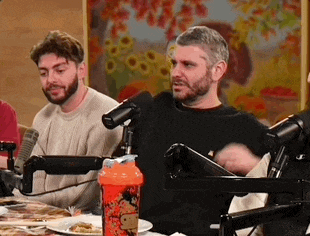 a group of men are sitting at a table with microphones and plates of food .