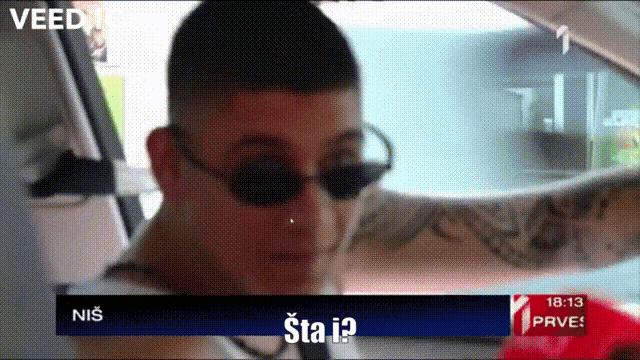 a man wearing sunglasses is sitting in a car with the time of 18:13 on the screen