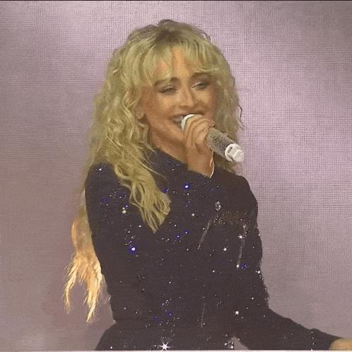 a blonde woman singing into a microphone with a purple background