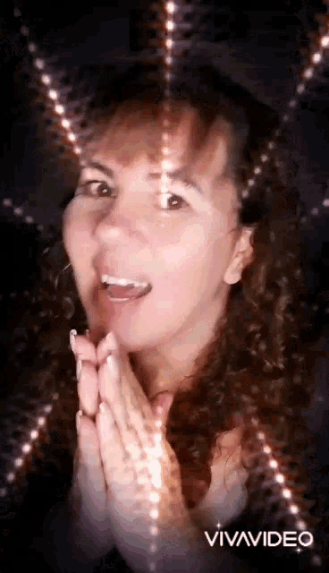 a woman with curly hair is making a funny face with her hands folded in prayer .
