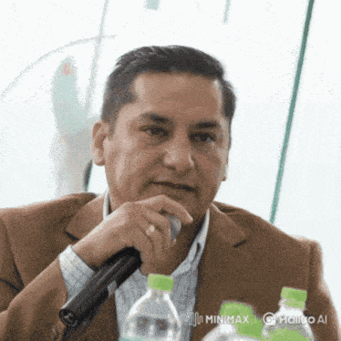 a man in a suit holds a microphone in front of bottles of water
