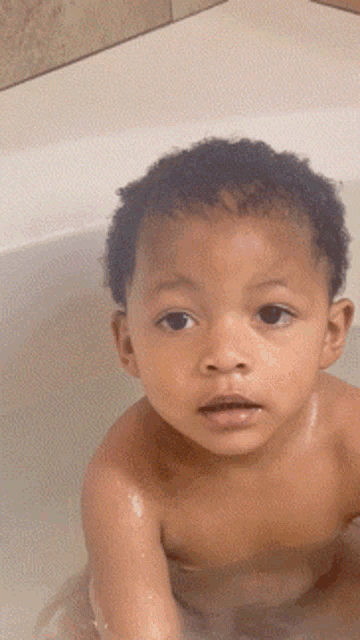 a young boy without a shirt is taking a bath in a bathtub