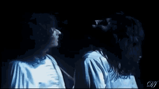 a man and a woman are standing next to each other in a dark room and looking at each other .