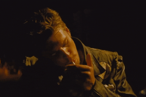 a man in a green jacket is lighting a cigarette in a dark room