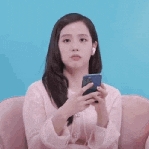 a woman in a pink shirt is sitting on a couch holding a cell phone .