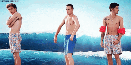 three shirtless men in swim trunks are standing on a beach near the ocean .