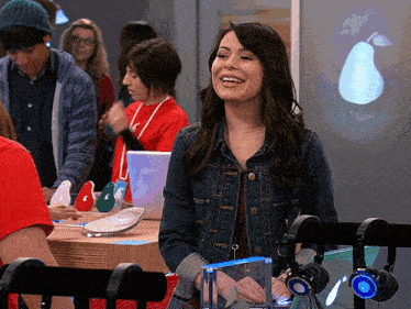 a woman in a denim jacket smiles while standing in front of headphones