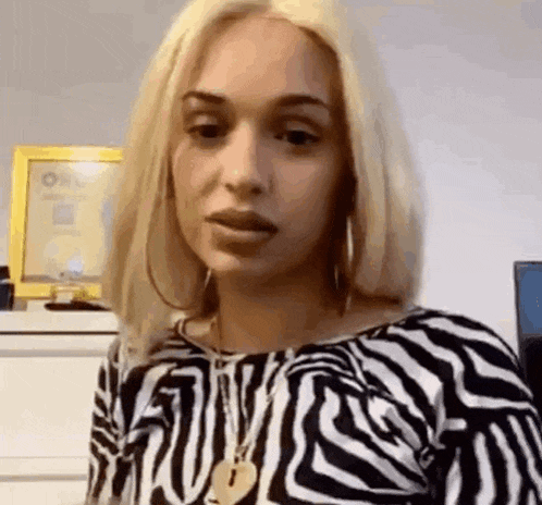 a woman with blonde hair is wearing a black and white zebra print shirt and earrings .