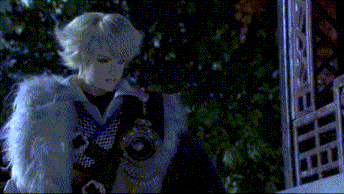 a doll with blonde hair and a white fur coat stands in front of a fence