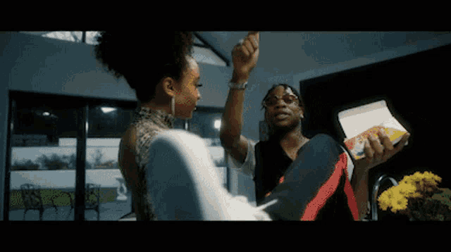 a man and a woman are dancing in a kitchen and the woman is holding a box of cereal .