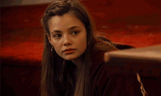 a young girl in a red sweater is sitting on the floor looking at the camera .