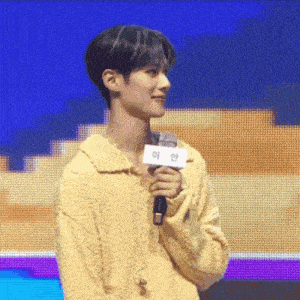 a man in a yellow sweater is holding a microphone in front of a large screen .