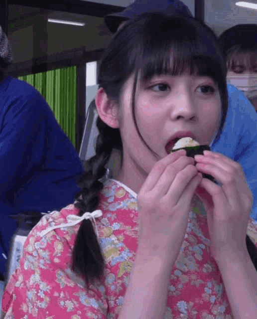 a woman in a pink dress is eating a piece of sushi