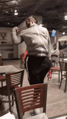a man is dancing in a restaurant with tables and chairs in front of him