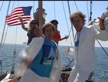 a group of people are dancing on a boat with an american flag behind them