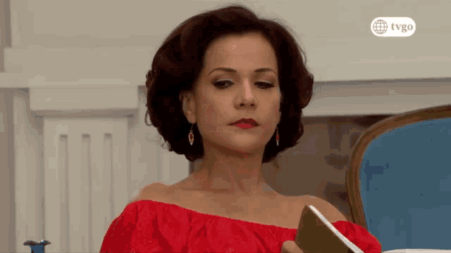 a woman in a red off the shoulder top is sitting in a blue chair reading a book