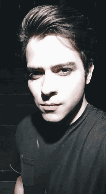 a young man in a black shirt takes a selfie in the dark